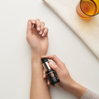 Person applying the peace serum product to their wrist on a light surface.